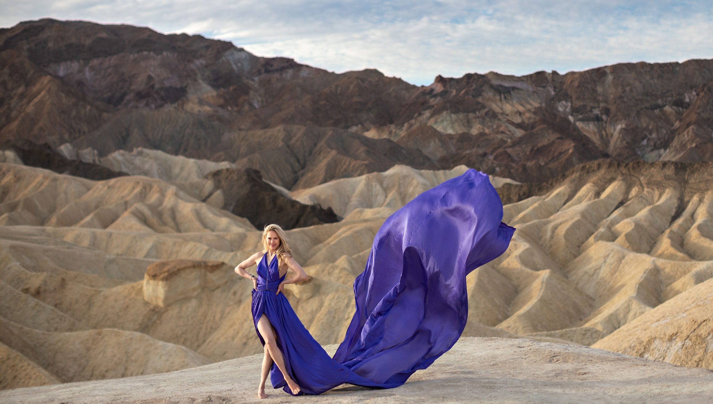 Woman in a long purple, dress with badlands and clouds.