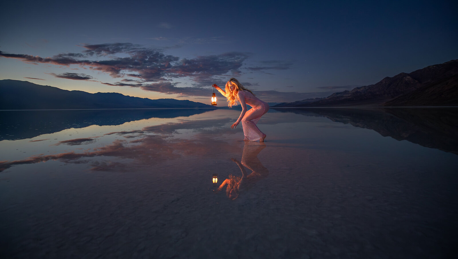 Woman standing in lake at night in a pink dress with mountains.