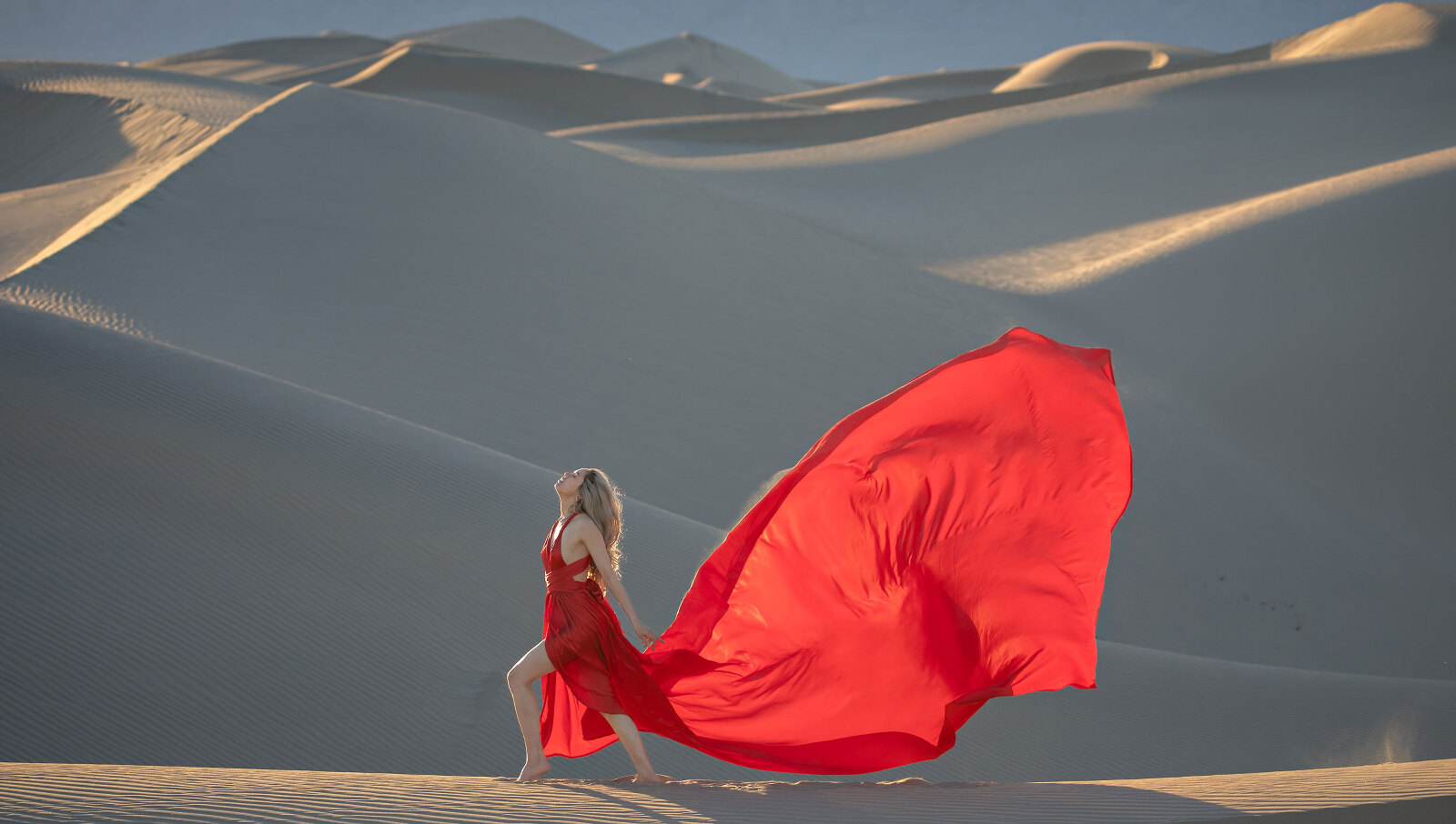 Woman on top of sand dune in a red, long dress.
