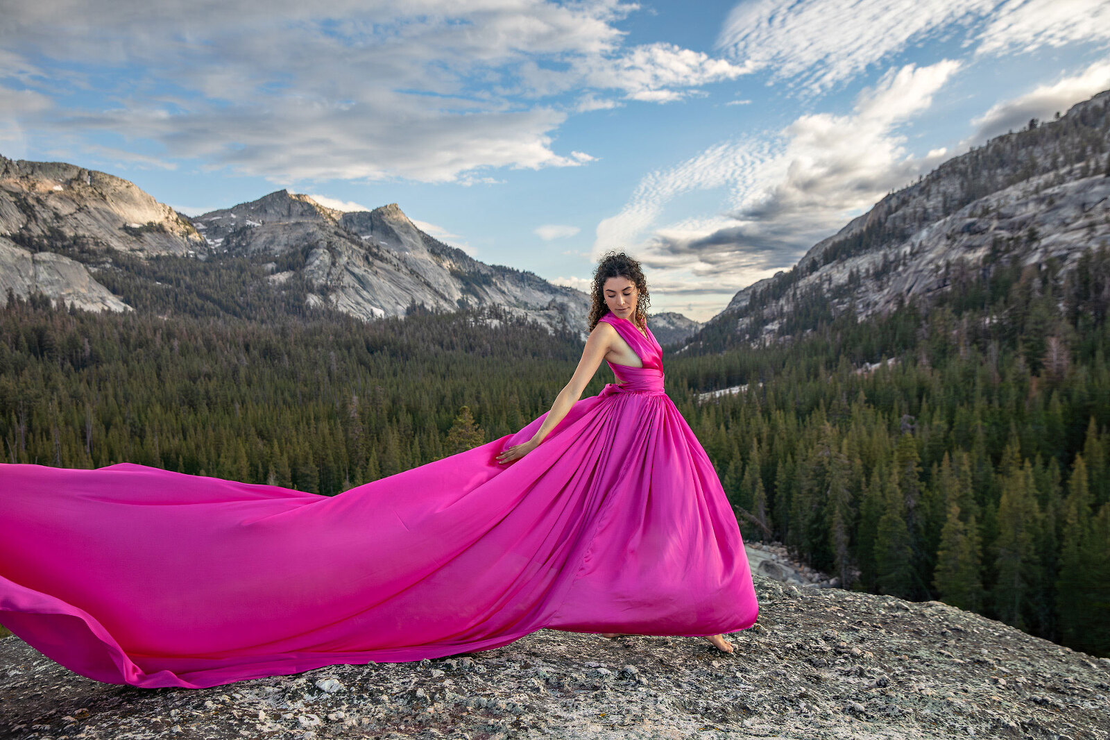 Woman on top of dome in a pink, long dress with mountains and clouds.