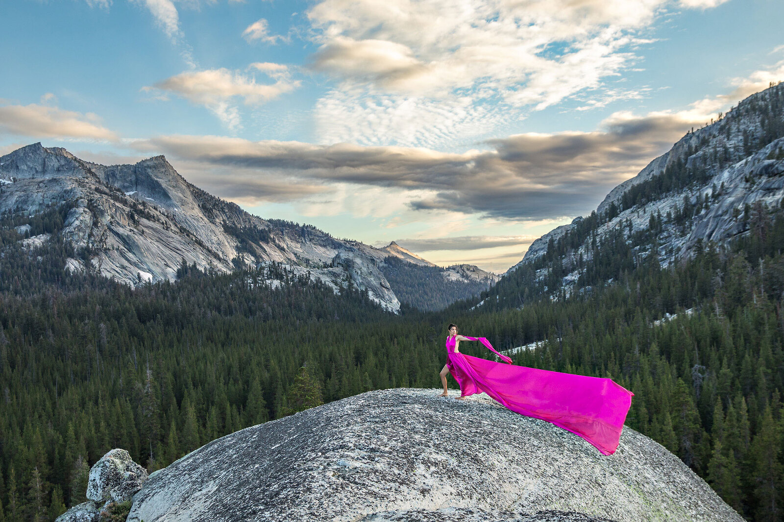 Woman on top of dome wearing a long, pink dress with mountains and clouds.