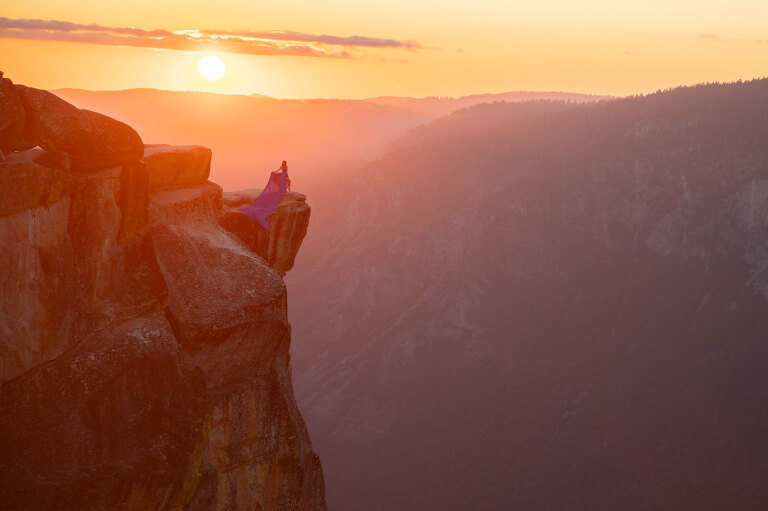 Woman on cliff during sunset wearing a long, blue dress.