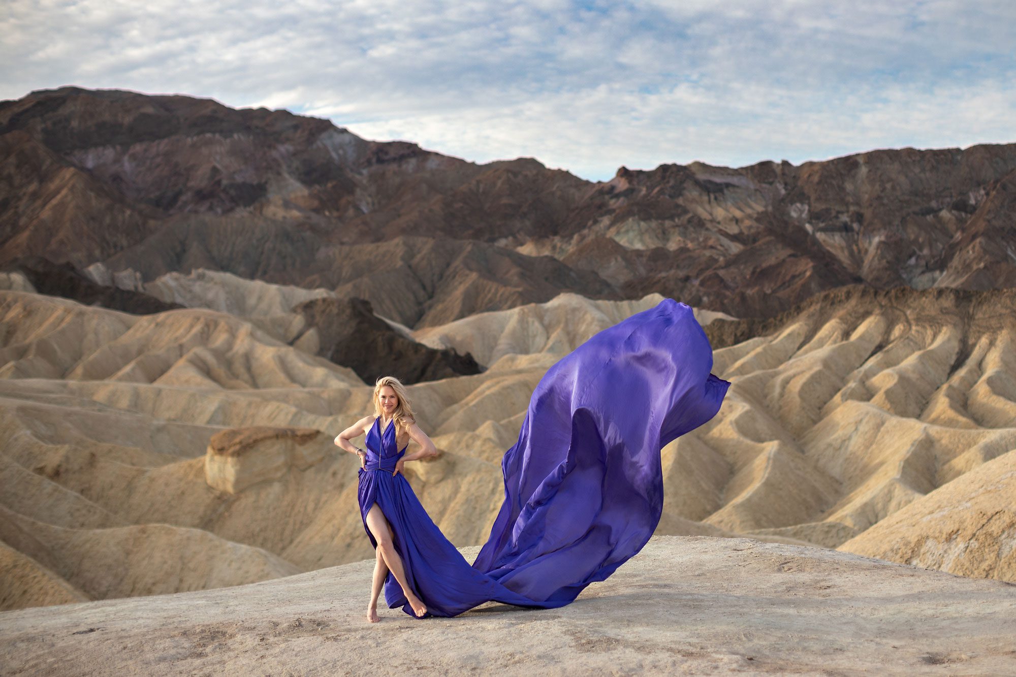 Woman standing at viewpoint with badlands and clouds.